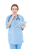 Thinking female doctor holding a tablet and looking into the camera
