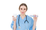 Young female doctor holding a plastic cup and medicine looking into the camera