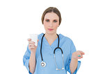 Female doctor holding a plastic cup and pills while looking into the camera