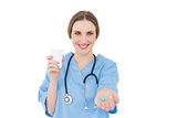 Pretty female doctor holding a plastic cup and handing blue pills