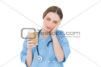 Female doctor holding a coffee mug and lifting her hand to her face with closed eyes
