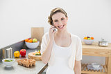 Joyful young woman phoning with her smartphone standing in kitchen