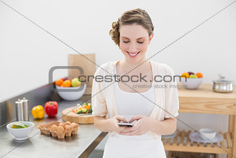 Cheerful young woman messaging with her smartphone standing in the kitchen