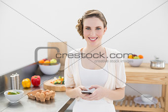 Peaceful lovely woman holding her smartphone standing in the kitchen
