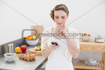 Thinking beautiful woman using her smartphone standing in the kitchen