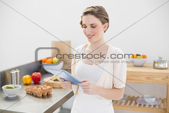 Smiling cute woman using her tablet standing in her kitchen