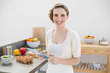 Happy gorgeous woman holding her tablet standing in her kitchen