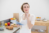 Thoughtful beautiful woman holding her tablet while standing in her kitchen