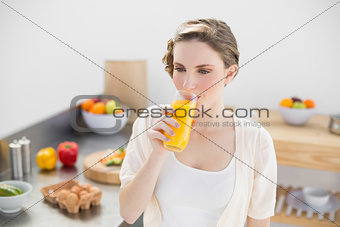 Lovely brunette woman drinking a glass of orange juice standing in her kitchen