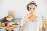 Gorgeous woman drinking a glass of orange juice standing in her kitchen