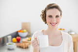 Smiling young woman posing in kitchen holding a cup