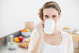 Beautiful woman drinking from cup standing in her kitchen