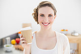 Content young woman holding a disposable cup standing in her kitchen