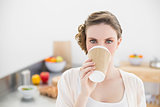 Beautiful woman drinking of disposable cup standing in kitchen
