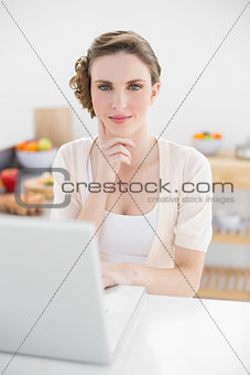 Thinking pretty woman sitting in kitchen using her notebook