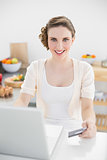 Happy beautiful woman using her notebook for home shopping sitting in kitchen