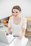Astonished gorgeous woman using her notebook for home shopping in her kitchen