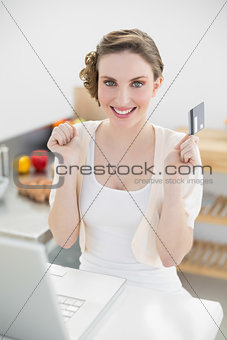 Happy brunette woman sitting in kitchen while home shopping
