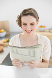 Fresh young woman reading newspaper sitting in her kitchen