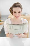 Content beautiful woman sitting in kitchen reading newspaper