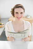 Gorgeous calm woman holding newspaper sitting in her kitchen at home