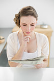 Young woman reading concentrated newspaper sitting in her kitchen