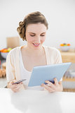 Pretty woman using her tablet for home-shopping while sitting in her kitchen
