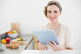 Happy beautiful woman holding her tablet sitting in her kitchen at home