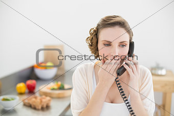 Astonished young woman phoning with her telephone in her kitchen