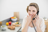 Amused lovely woman sitting in her kitchen phoning with a telephone