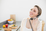 Laughing beautiful woman phoning with a telephone in her kitchen