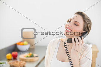 Laughing beautiful woman phoning with a telephone in her kitchen