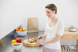 Cheerful young woman cutting vegetables while standing in her kitchen