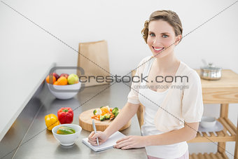 Lovely woman standing in her kitchen writing a shopping list
