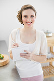 Young woman standing in her kitchen writing a shopping list smiling at camera