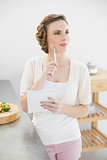 Thinking woman standing in kitchen writing a shopping list
