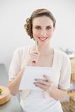 Cheerful woman thinking while writing the shopping list in her kitchen