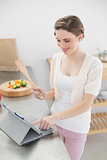 Smiling brunette woman using her tablet while standing in her kitchen