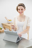 Smiling brunette woman standing in her kitchen while working with her tablet