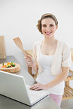 Happy cute woman using her laptop standing in the kitchen