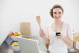 Cheerful woman holding her smartphone standing in the kitchen