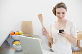 Content brunette woman using her smartphone standing in the kitchen