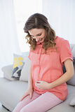 Cheerful pregnant woman sitting in the living room on a couch