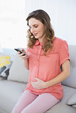 Calm pregnant woman using her smartphone sitting on a couch in the living room