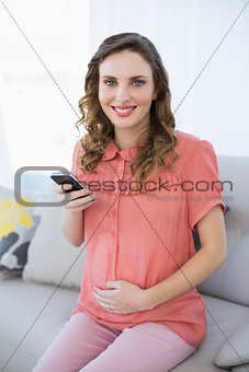 Content calm pregnant woman holding her smartphone sitting on couch