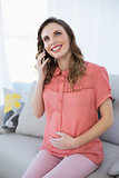 Happy calm pregnant woman phoning with her smartphone sitting in the living room
