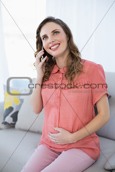 Happy calm pregnant woman phoning with her smartphone sitting in the living room