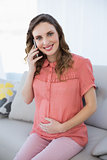 Young pregnant woman phoning with her smartphone sitting in the living room on a couch