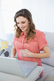 Smiling pregnant woman using her notebook while sitting on couch in the living room