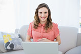 Cheerful pregnant woman using her notebook while sitting on couch